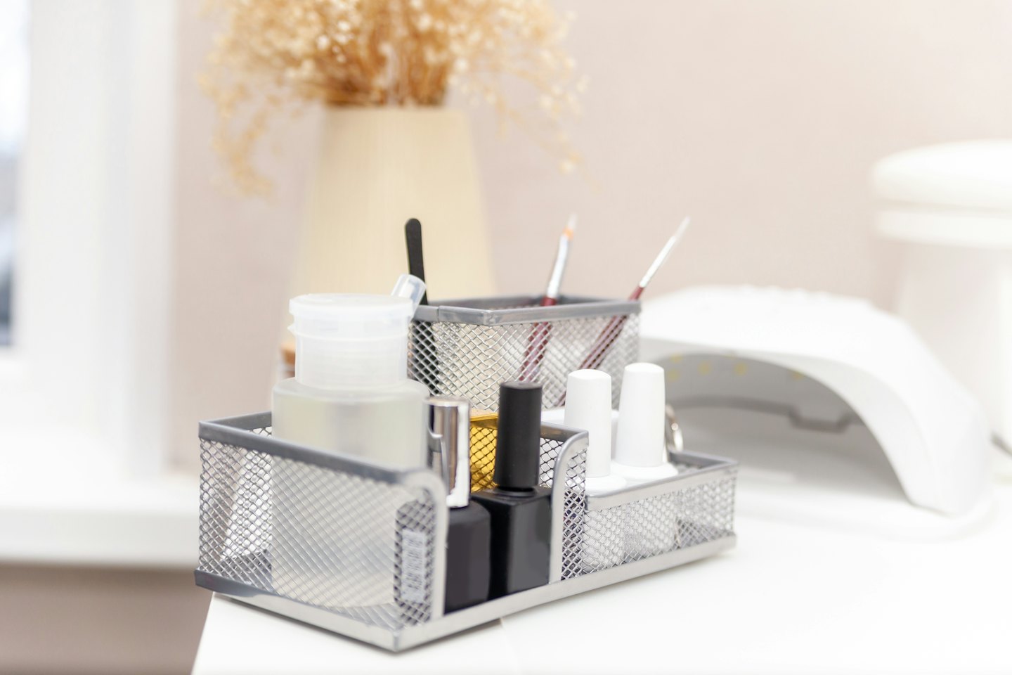 Organizzatore in rete metallica pieno di vari articoli per nail art su un tavolo.